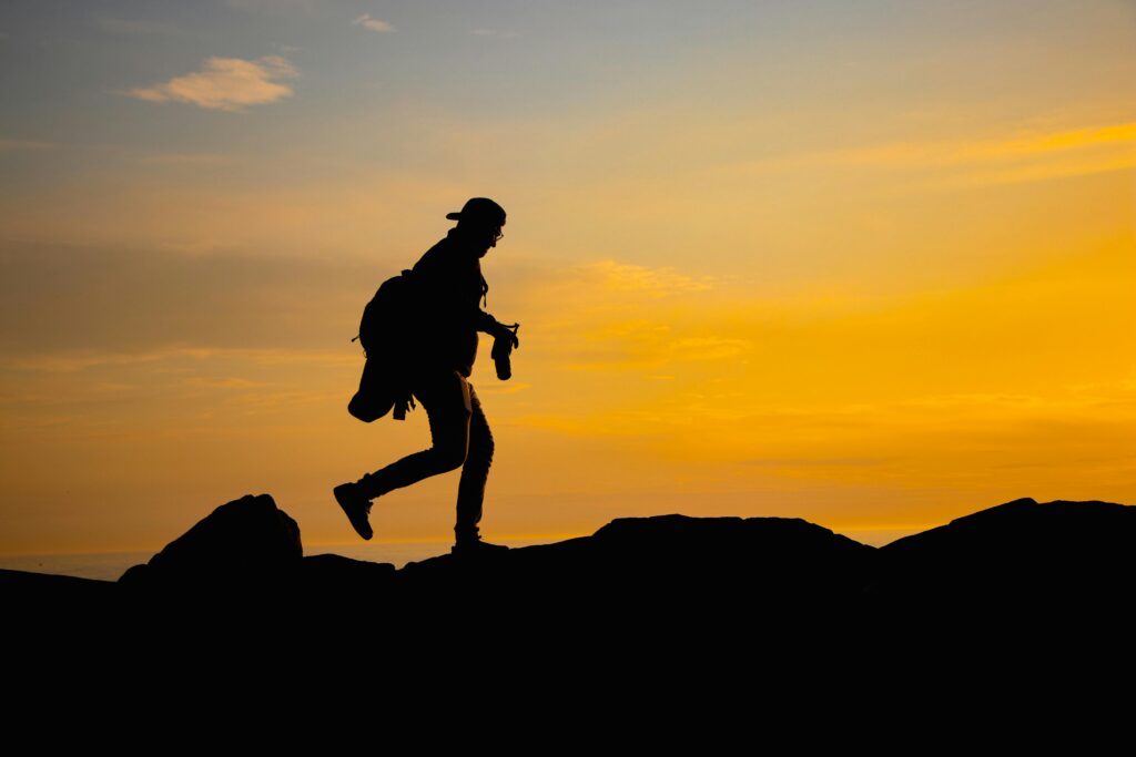 A dramatic silhouette of a man hiking over rocks at sunset, capturing outdoor adventure.